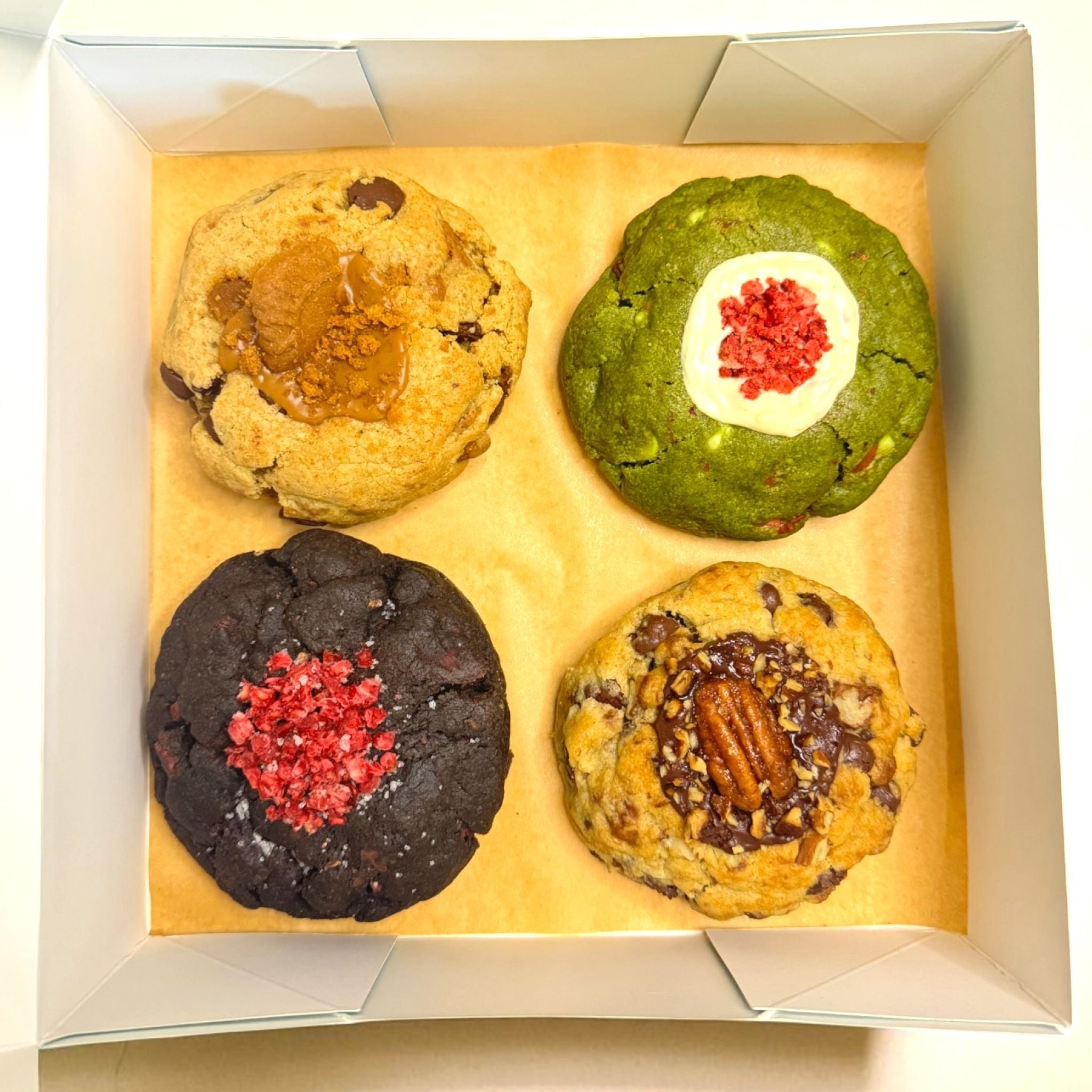 Top down view of an open regular assortment cookie box from Le Petit Cookie with four assorted gourmet cookies inside.