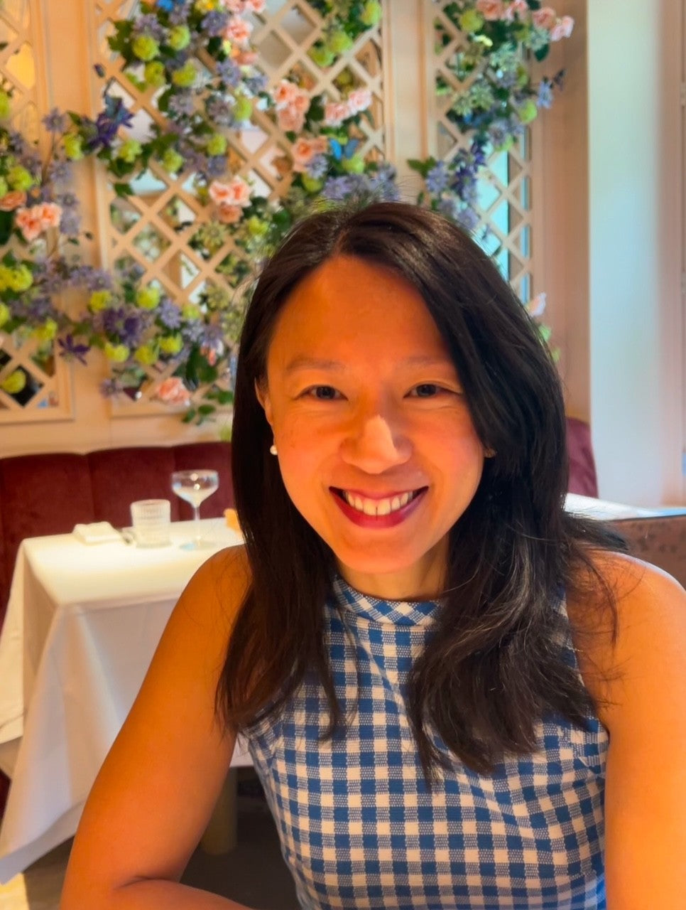 Le Petit Cookie founder, Monique, in a blue checkered dress sitting in a decorated restaurant setting.