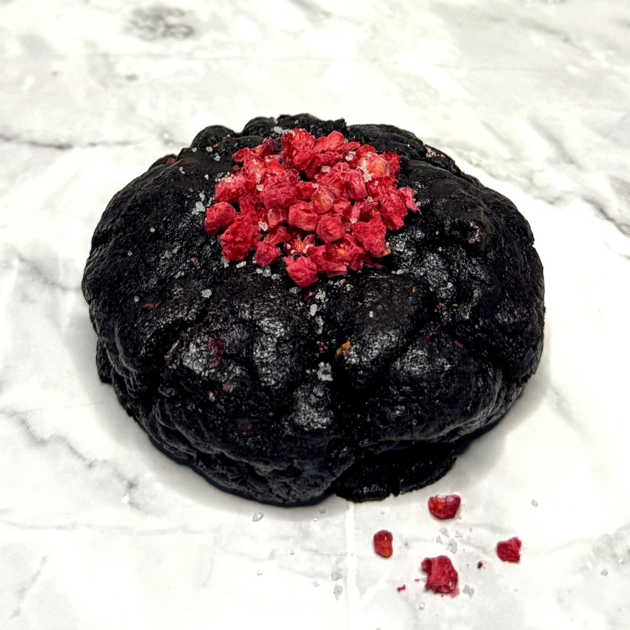 Front view of a Midnight Berry Cookie with Valrhona® raspberry chips, fleur de sel and dried raspberries on a marble countertop.