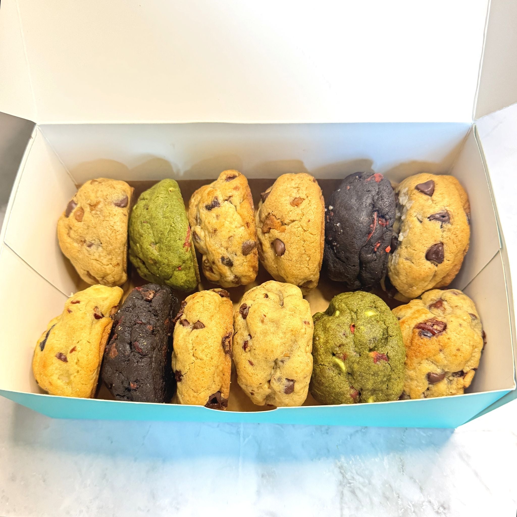 A top down view of an open petit assortment box from Le Petit Cookie showcasing a variety of 12 different gourmet petit cookies.