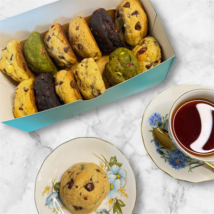 A petit assortment cookie box from Le Petit Cookie featuring 12 assorted gourmet cookies in a cookie box next to a cup of tea on a marble countertop.