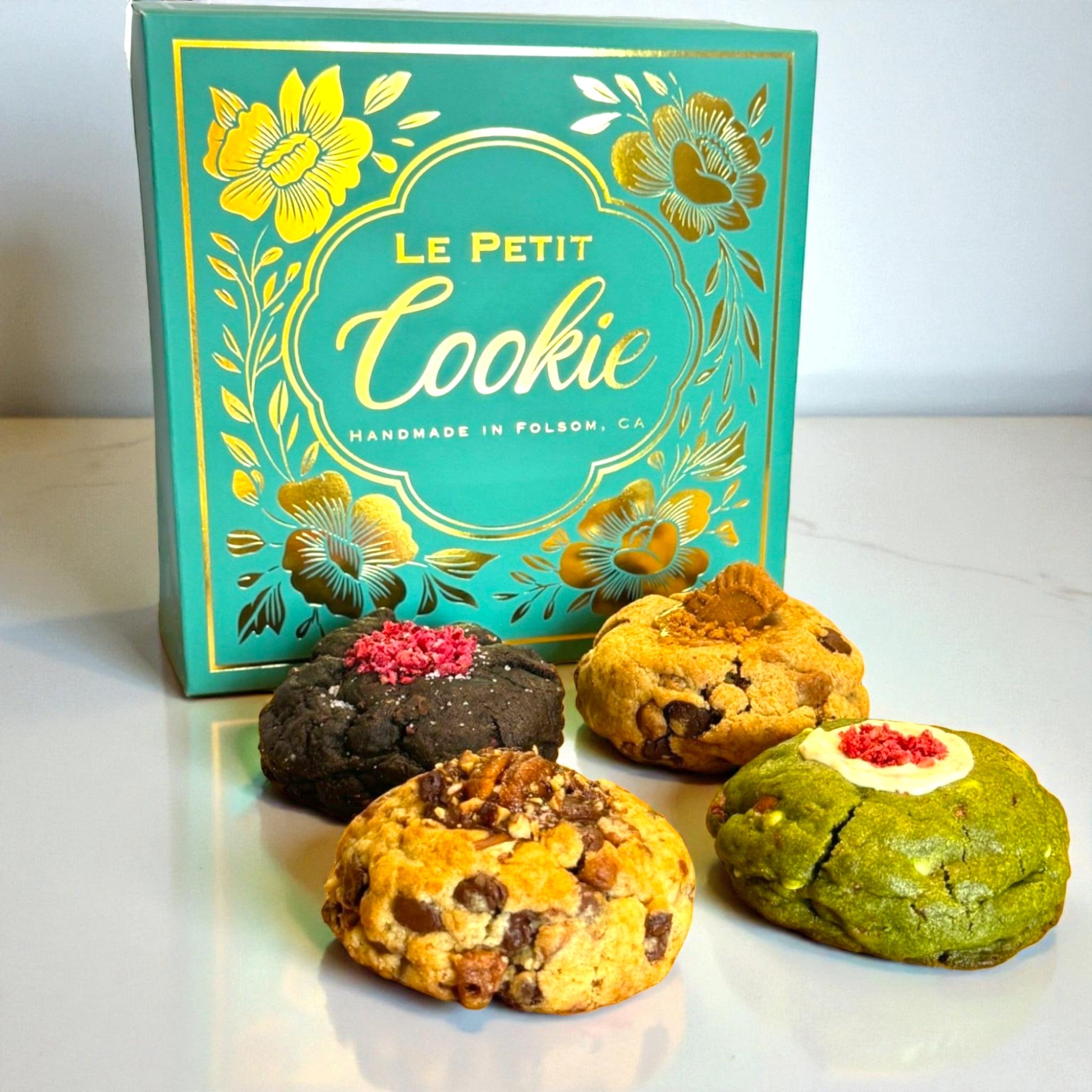 A Le Petit Cookie regular assortment cookie box with four assorted gourmet cookies on a marble countertop.