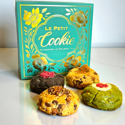 A Le Petit Cookie regular assortment cookie box with four assorted gourmet cookies on a marble countertop.