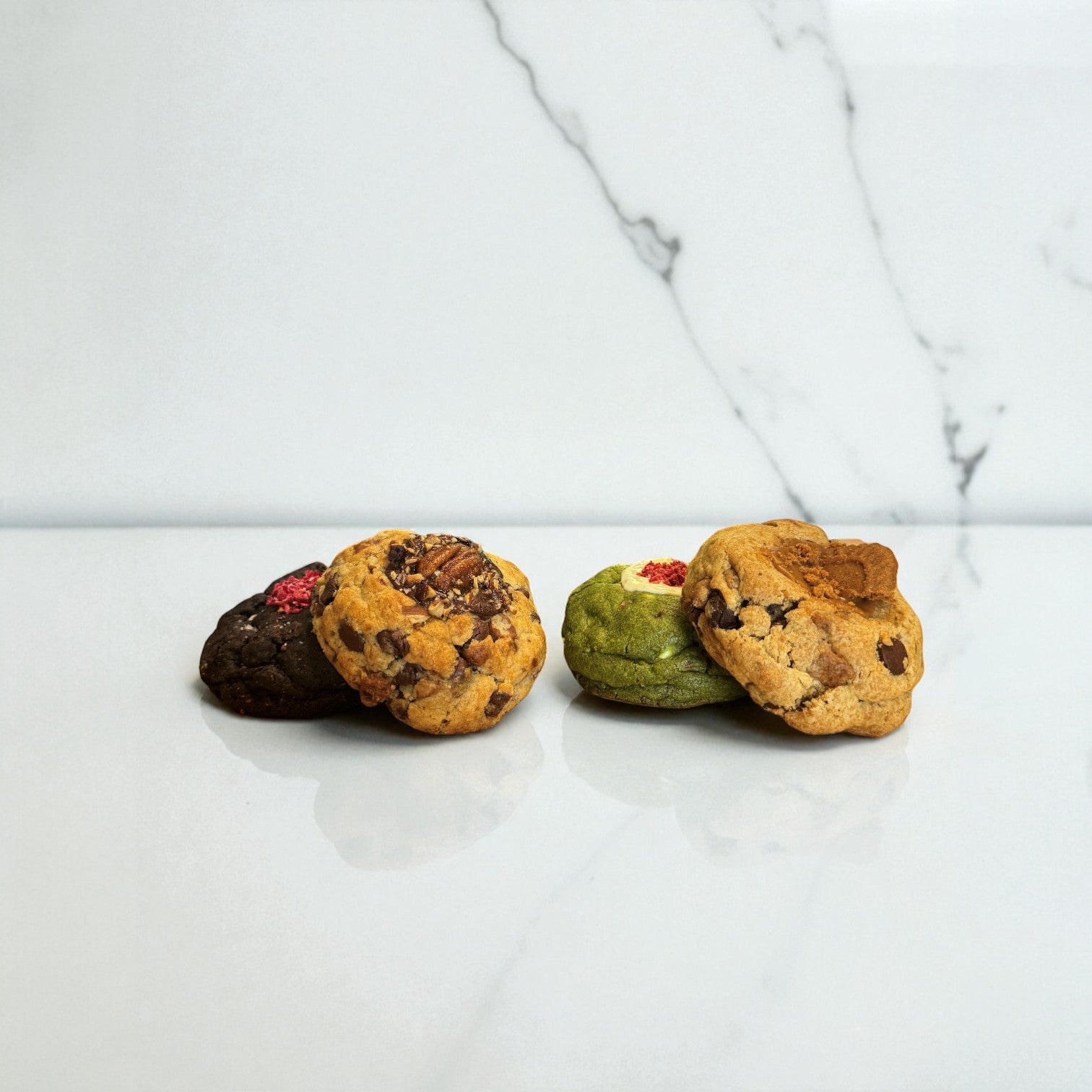 Four different regular gourmet cookies from Le Petit Cookie on a marble countertop