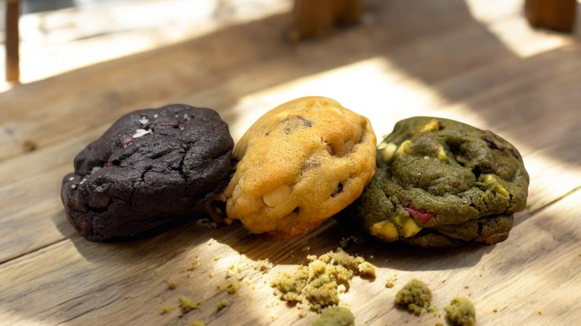 Three signature gourmet cookies from Le Petit Cookie on a wooden tabletop.