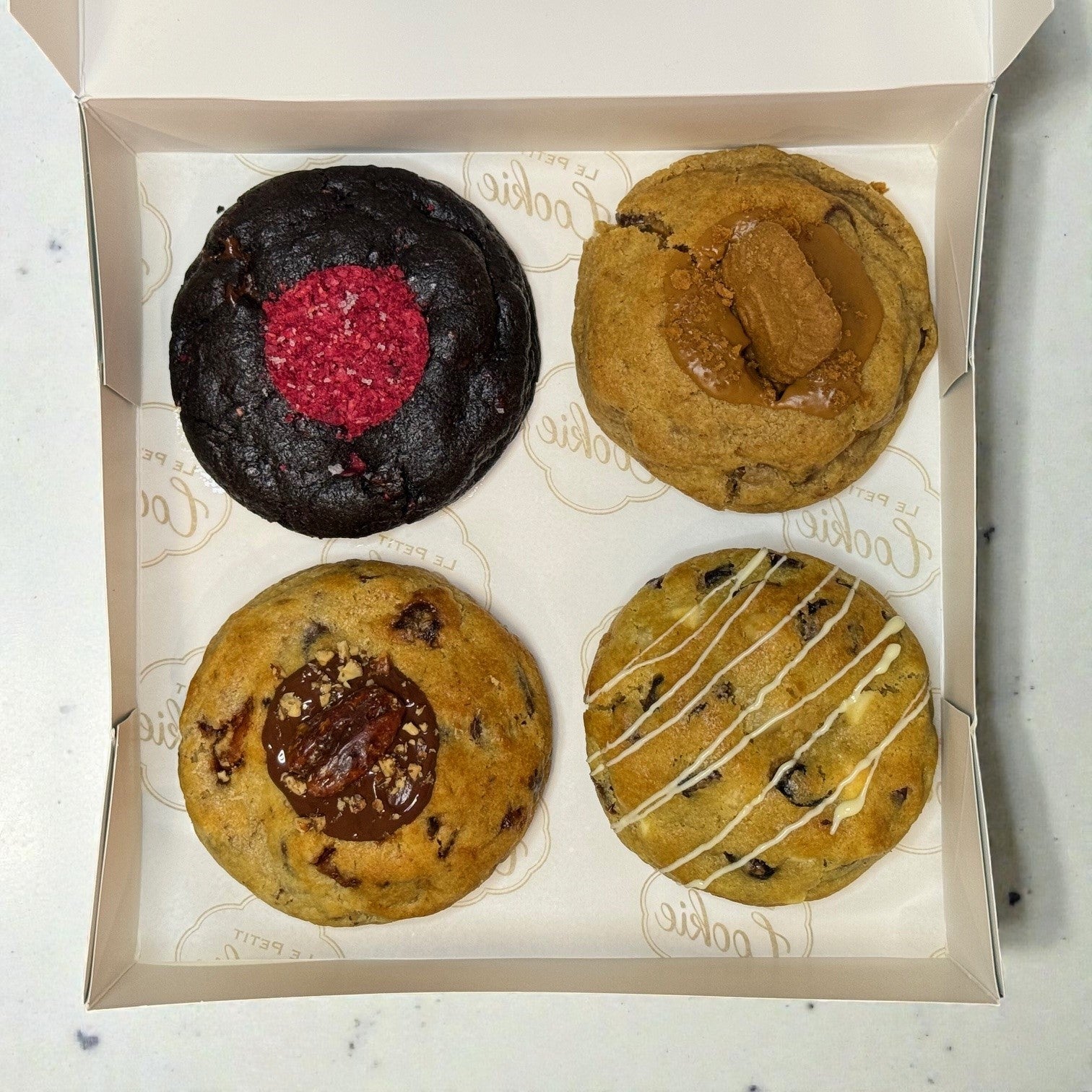 Monique’s Favorites Cookie Box containing four cookies: Midnight Berry, Scarlet Zest, Golden Banane, and Amber Dusk, neatly arranged inside the box.