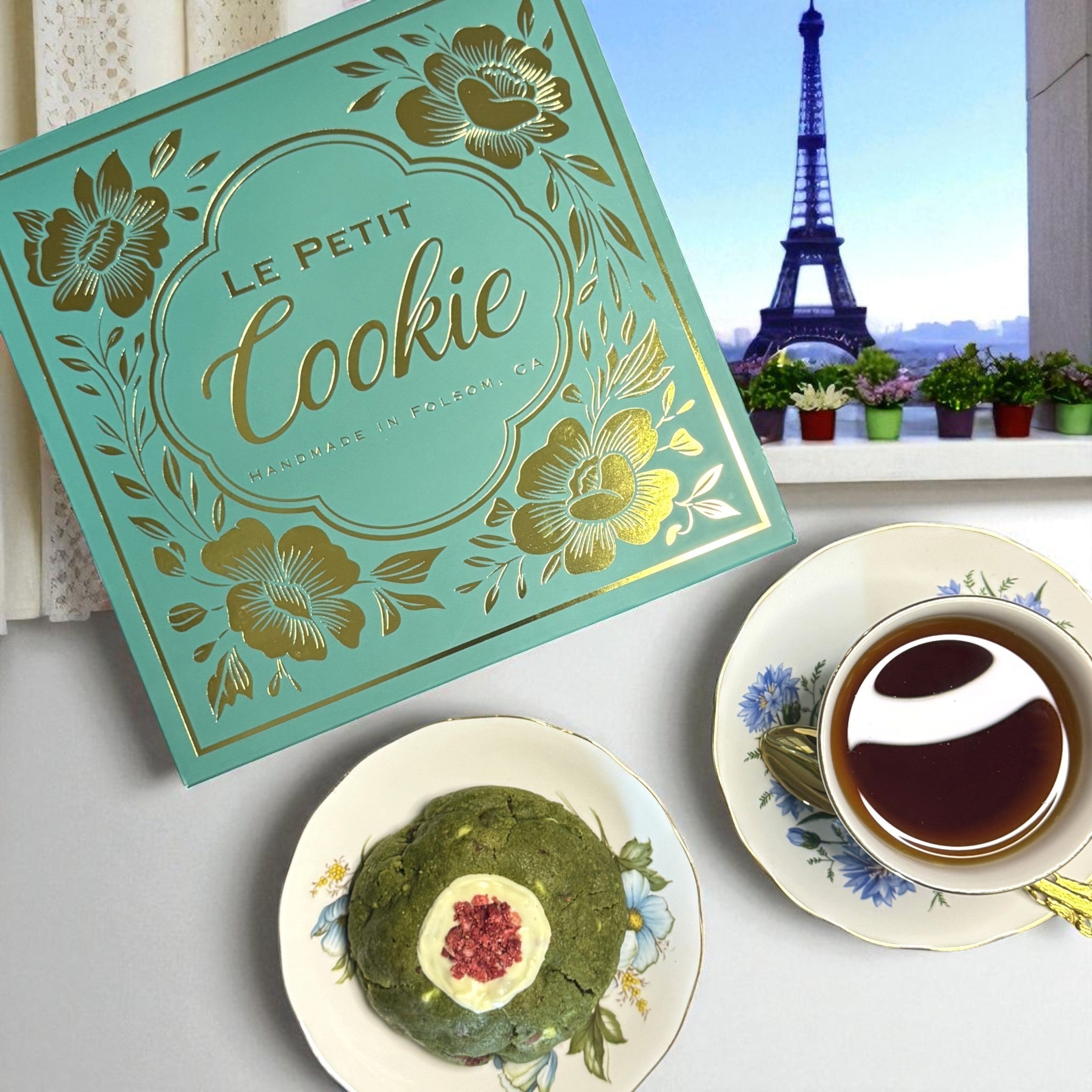 Tea cup with cookies on a saucer, 'Le Petit Cookie' box, and Eiffel Tower in the background